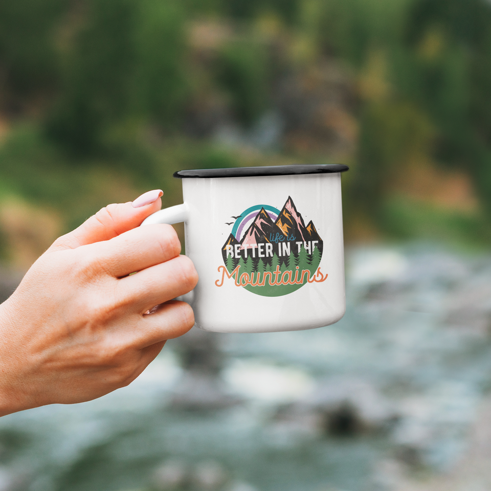 Hand holding enamel mug Better in the mountains